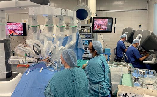 Robotic theatre set-up with the da Vinci Xi system: surgeon and trainee at joint consoles remote from the operating table, with the surgical assistant and scrub nurse at the bedside